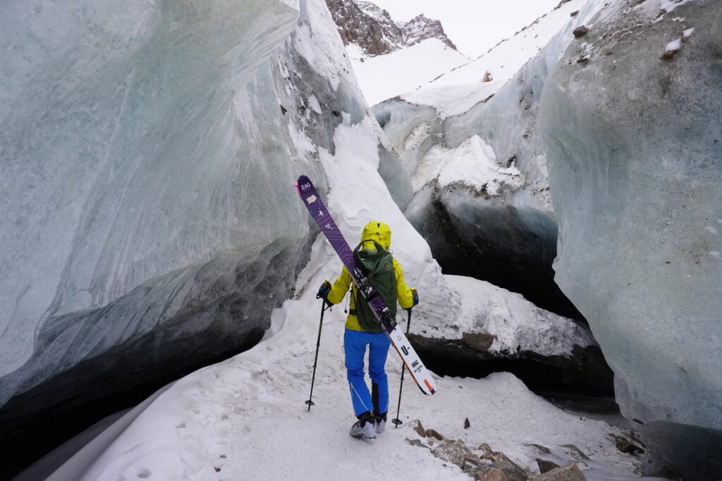 Skitourengeher mit Ski auf dem Rücken zwischen blauen Eisbrüchen eines Gletschers im Tien Shan bei Almaty