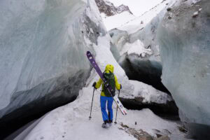 Skitourengeher mit Ski auf dem Rücken zwischen blauen Eisbrüchen eines Gletschers im Tien Shan bei Almaty