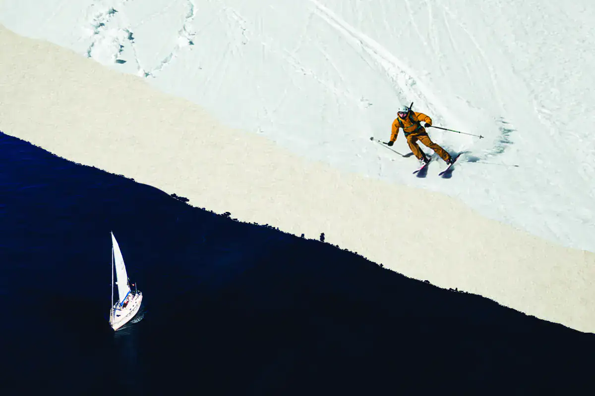 Luftaufnahme eines Skifahrers am verschneiten Ufer mit Segelboot im Fjord