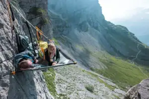Person liegt im Portaledge an einer Felswand über einem Alpental