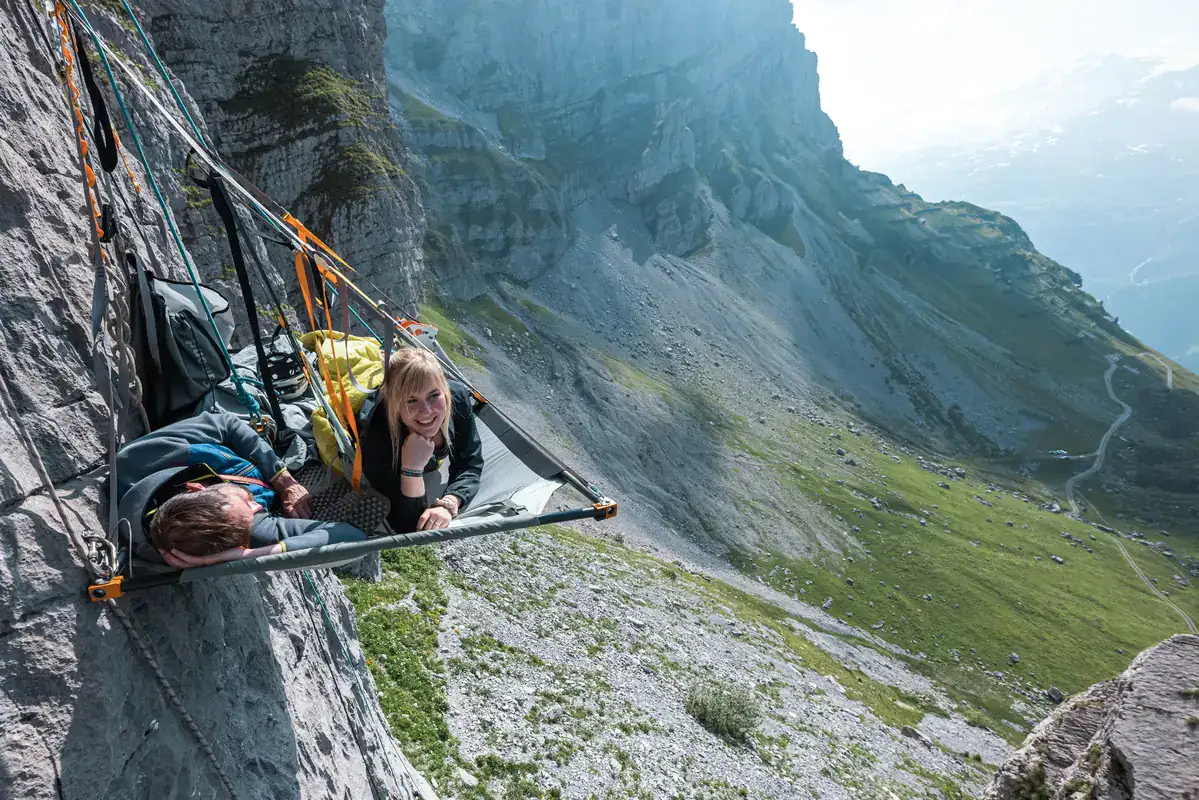 Person liegt im Portaledge an einer Felswand über einem Alpental