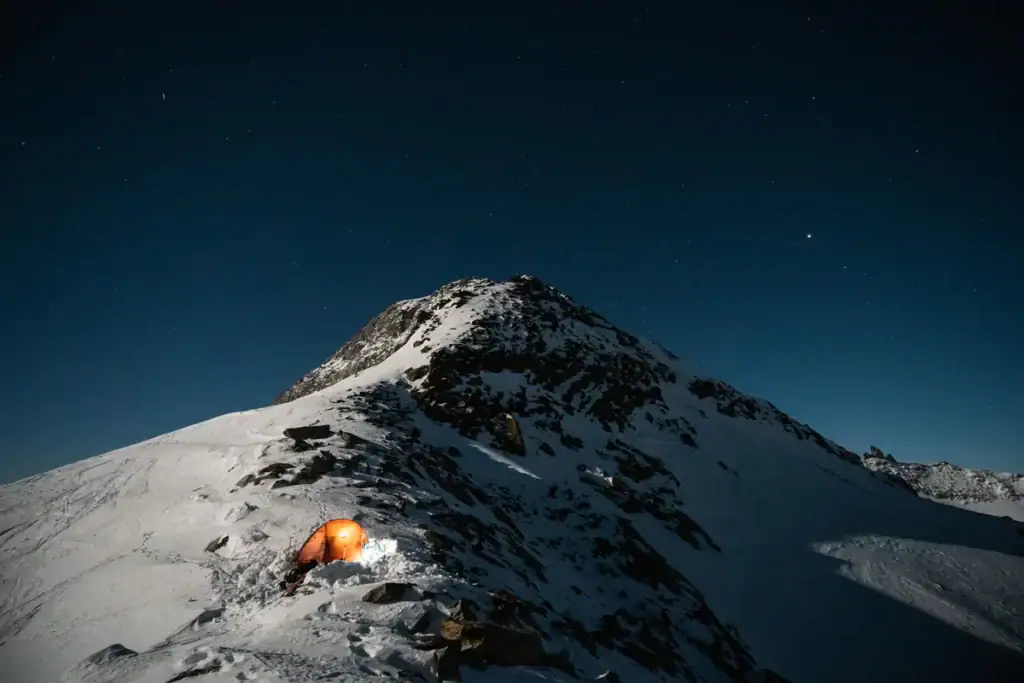 Beleuchtetes Zelt auf einem verschneiten Grat bei Nacht