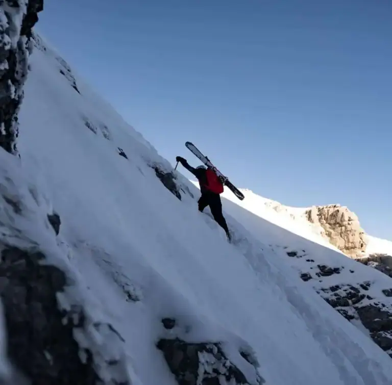 Skitourengeher mit Ski am Rucksack in einer steilen Schneeflanke