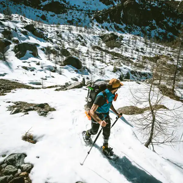 Schneeschuhwanderer mit grossem Rucksack im Aufstieg durch ein verschneites Tal