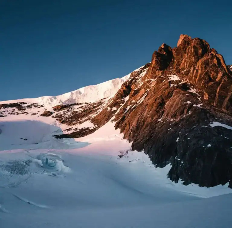 Vom Abendlicht rot gefärbter Felsgipfel über einem Gletscherplateau