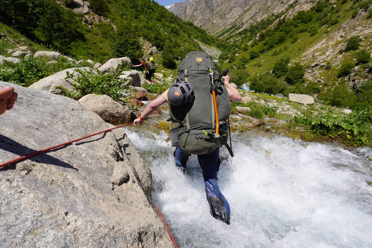 Trekker bei einer gesicherten Bachquerung im Fann-Gebirge