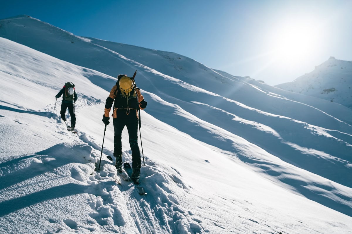 Zwei Skitourengeher spuren im Gegenlicht durch tiefen Schnee