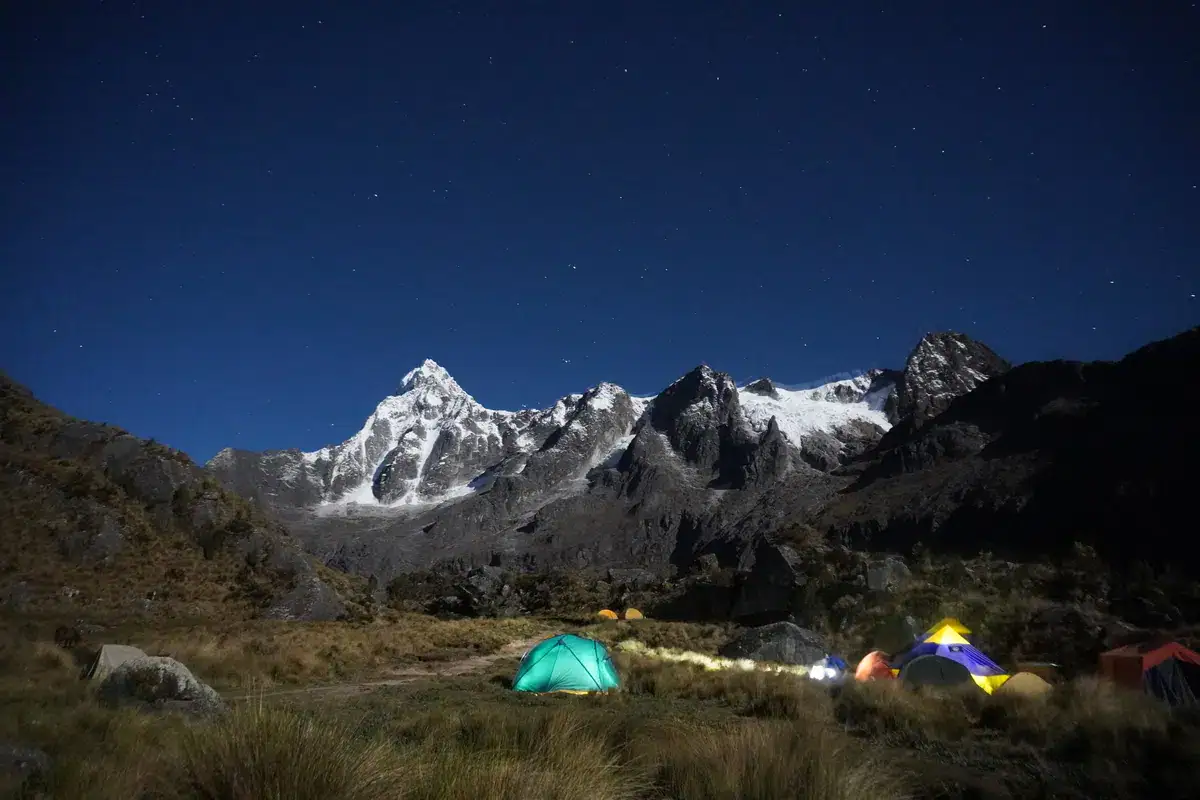 Beleuchtete Zelte eines Camps unter Sternenhimmel vor den vergletscherten Gipfeln der Cordillera Huayhuash