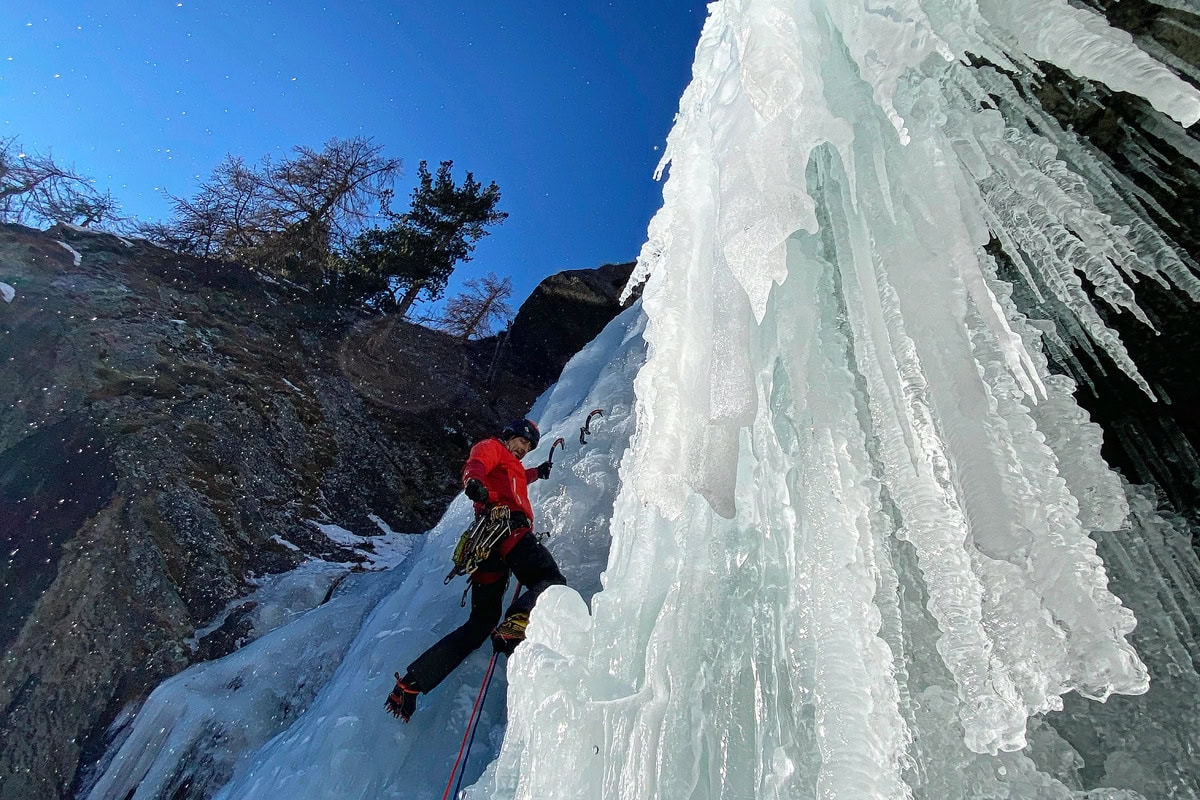 Eiskletterer in roter Jacke an einem breiten gefrorenen Wasserfall bei Cogne