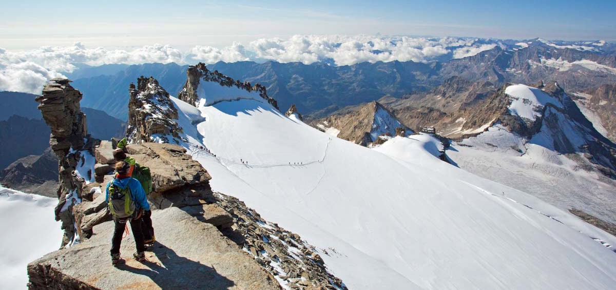 Zwei Bergsteiger auf dem felsigen Gipfelgrat des Gran Paradiso über dem Gletscherplateau
