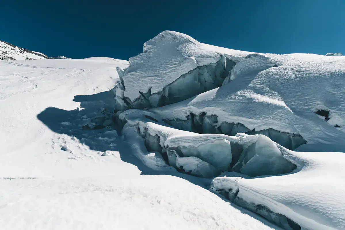 Aufgebrochene Gletscherspalten im Firn unter blauem Himmel