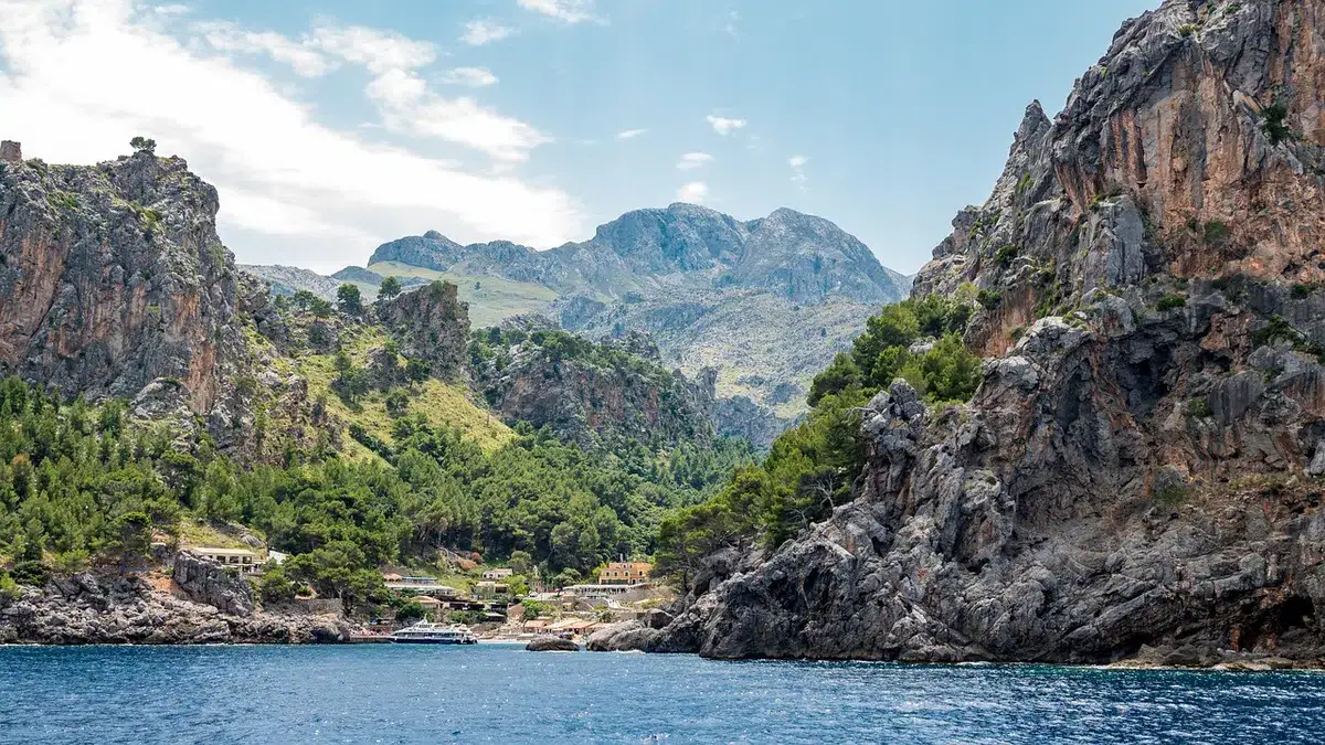 Zerklüftete Felsküste einer Bucht auf Mallorca mit dem Tramuntana-Gebirge im Hintergrund