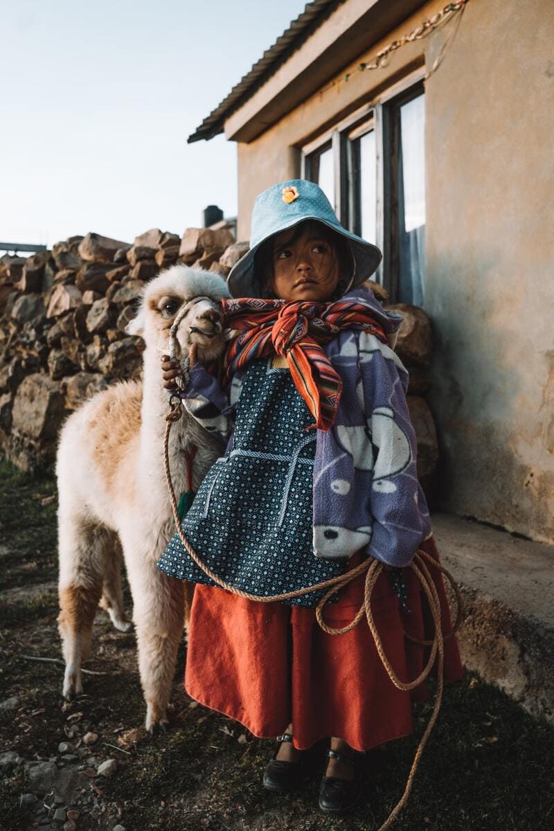 Mädchen in traditioneller Kleidung mit einem jungen Lama im bolivianischen Hochland