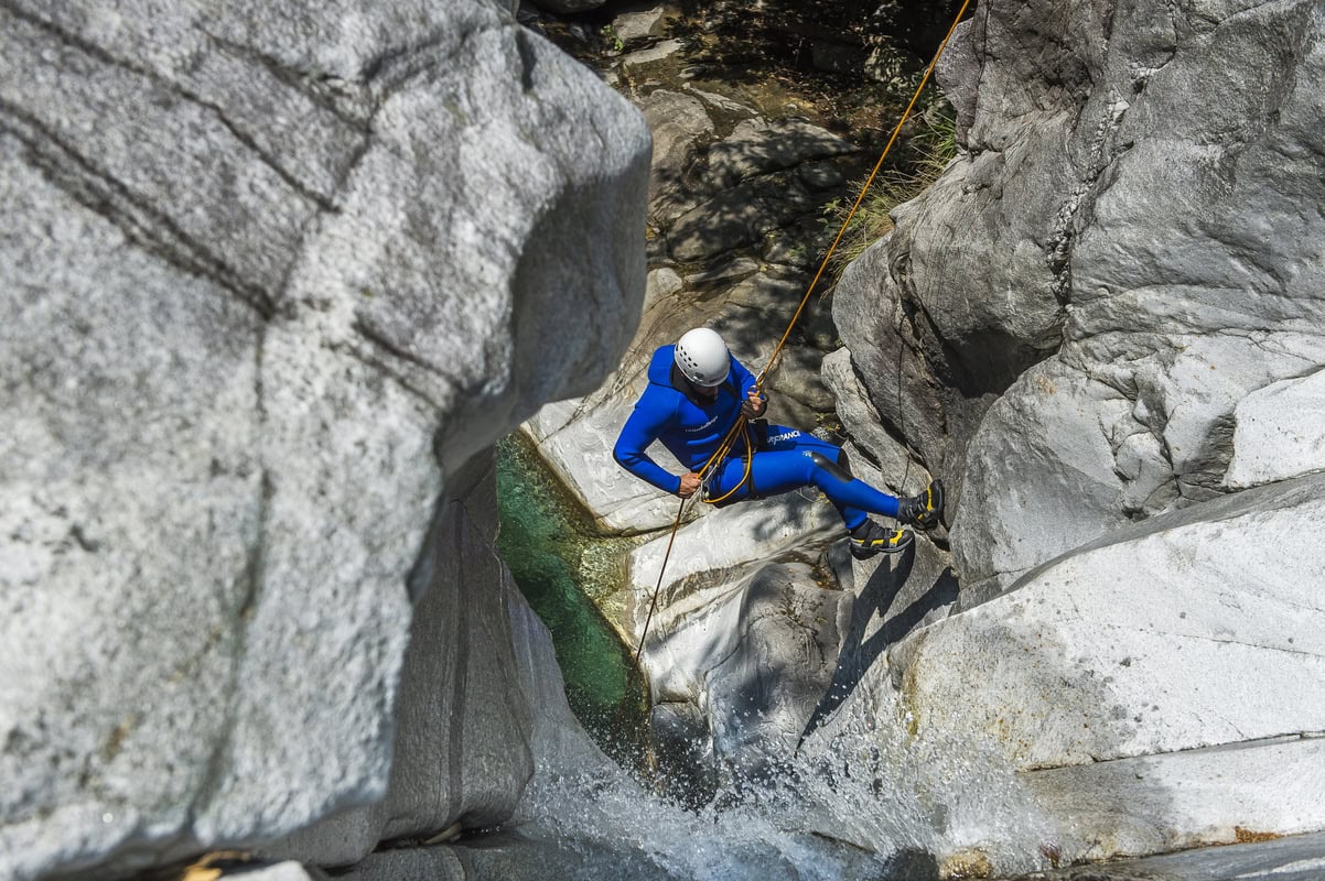 Person seilt sich beim Canyoning neben einem Wasserfall in eine Schlucht ab