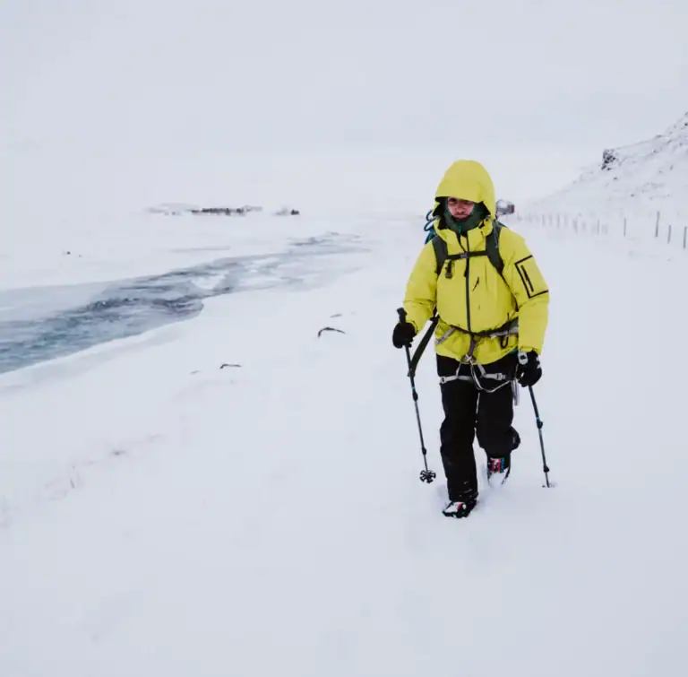 Wanderin in gelber Jacke mit Trekkingstöcken in verschneiter Küstenlandschaft