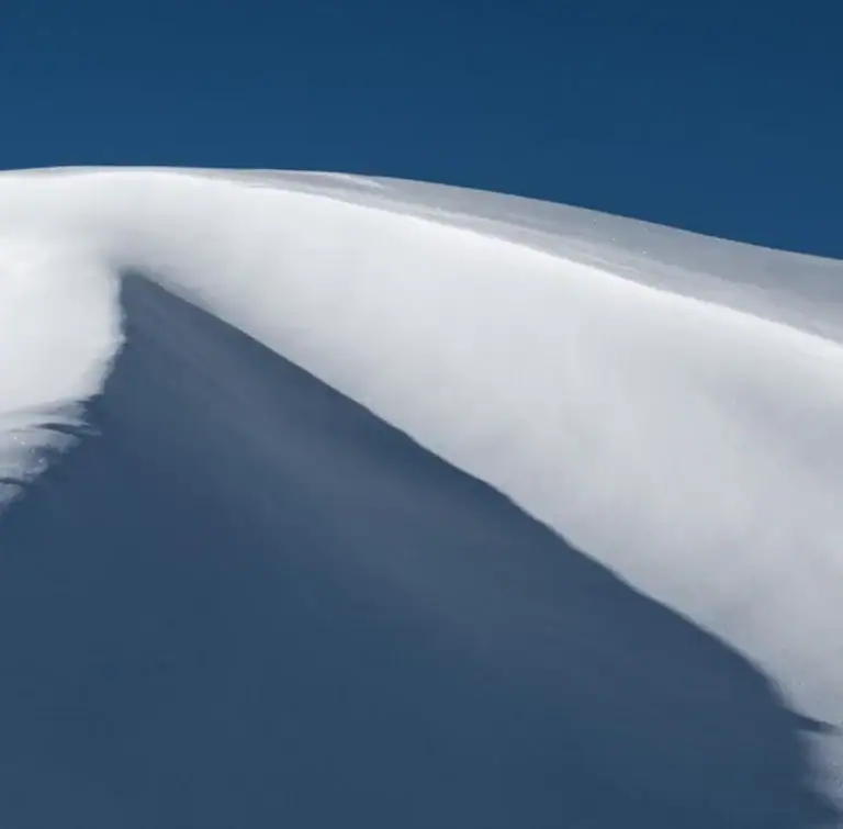Vom Wind geformte Schneewechte auf einem Grat vor tiefblauem Himmel