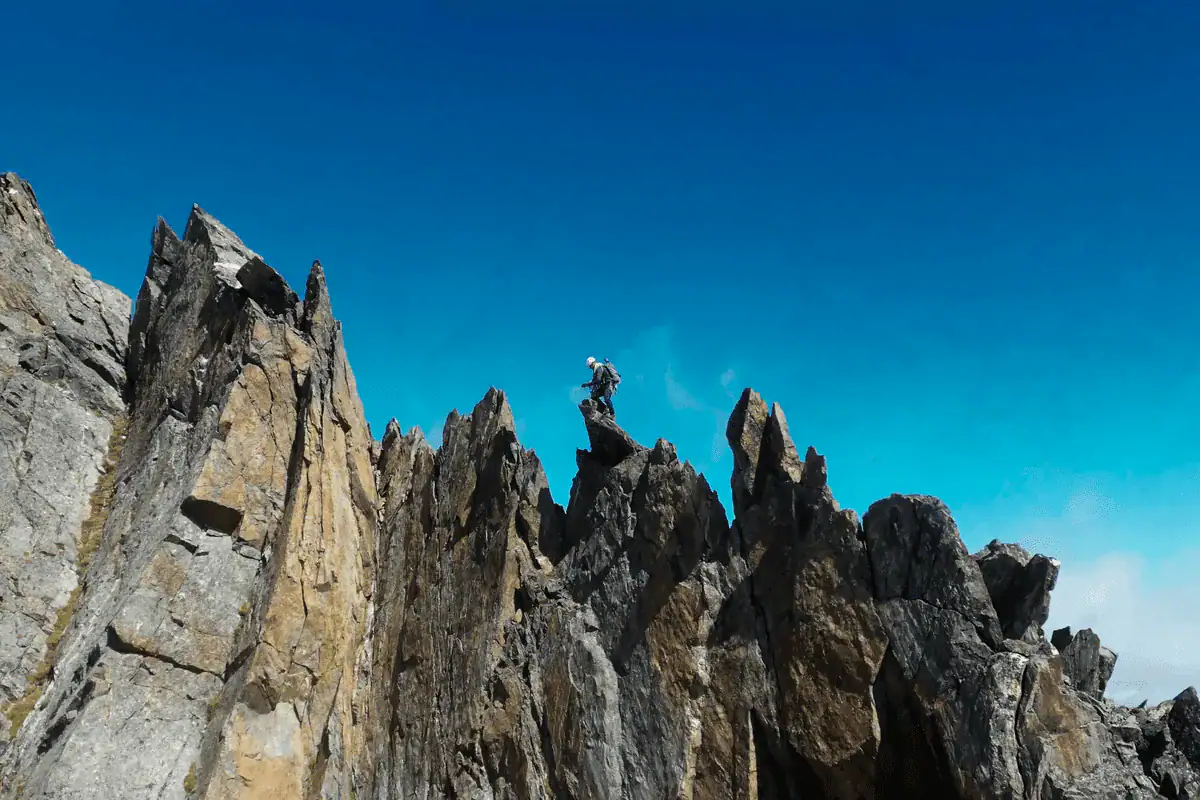 Alpinist auf einem gezackten Felsgrat vor blauem Himmel