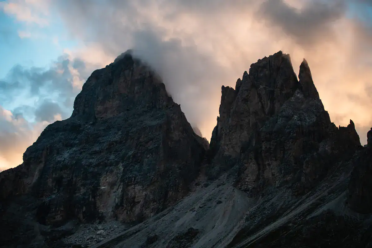 Dunkle Dolomitentürme im Abendlicht mit Wolken über den Gipfeln