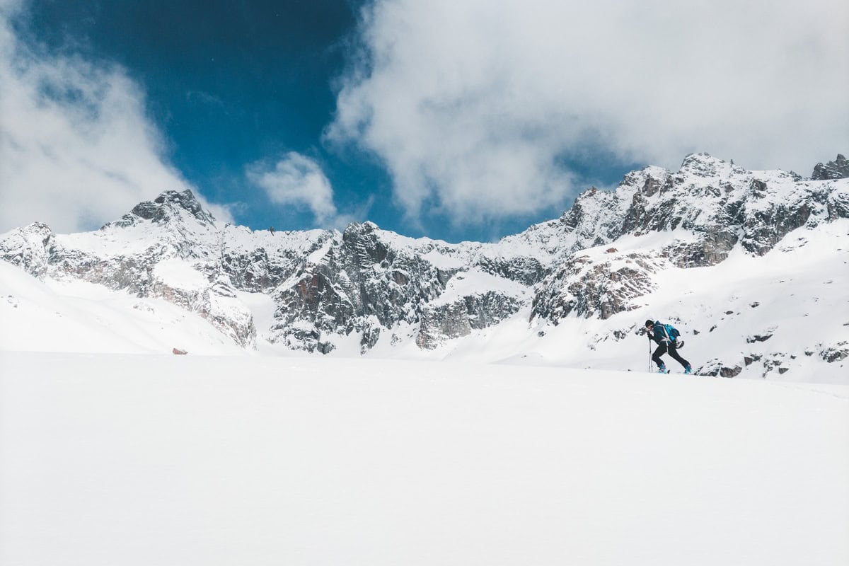 Skitourengeher spurt durch ein weites Schneefeld unter Felsgipfeln
