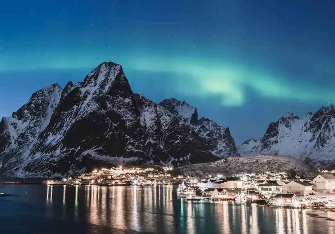 Fischerdorf auf den Lofoten bei Nacht mit Polarlicht über verschneiten Bergen