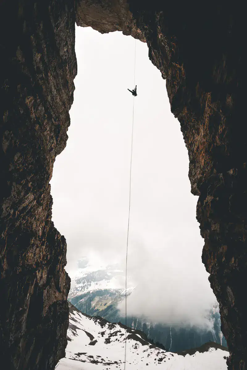 Kletterer am Seil in einer Felsschlucht mit Blick auf verschneite Berge