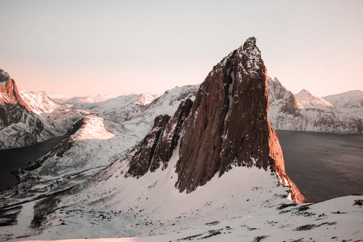 Der Felsgipfel Segla auf der Insel Senja im rosa Morgenlicht über dem verschneiten Fjord