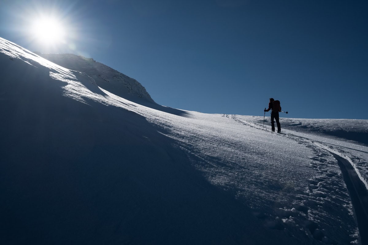 Einzelner Skitourengeher im Aufstieg auf einem sonnigen Schneerücken