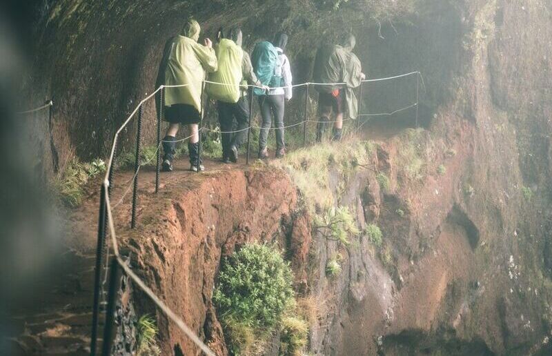 Wandergruppe in Regenkleidung auf einem gesicherten Felspfad im Nebel